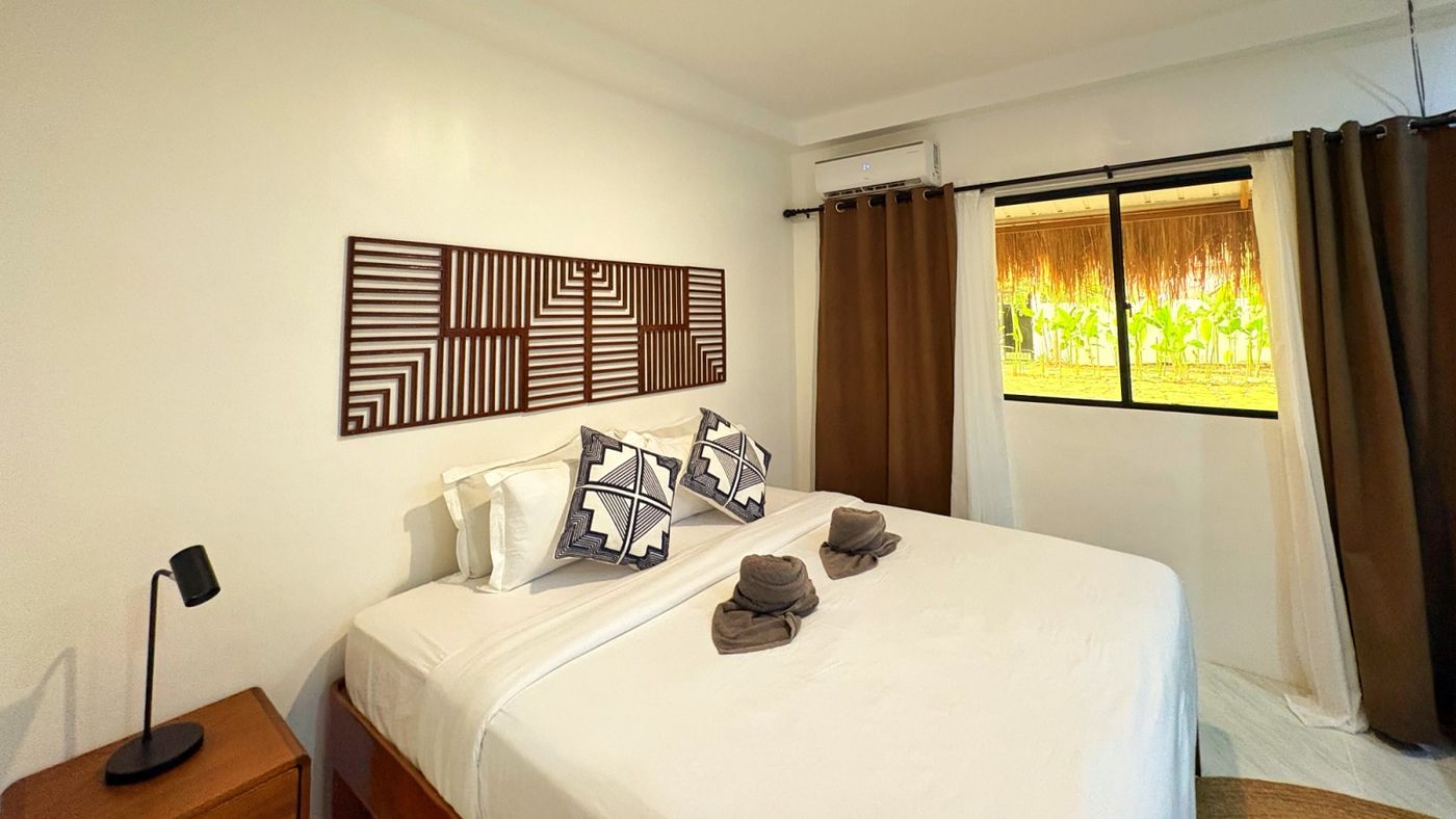 Bedroom with a white bed, a carved timber wall panel and a garden-facing window