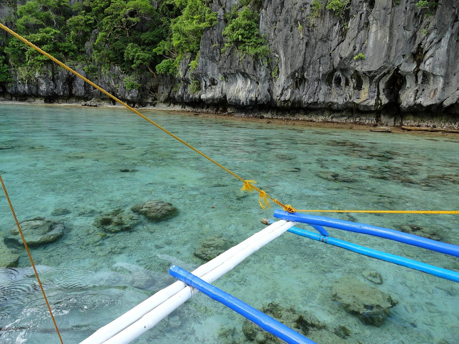 Clear water over coral and the blue outriggers of a banca, Big Lagoon, El Nido