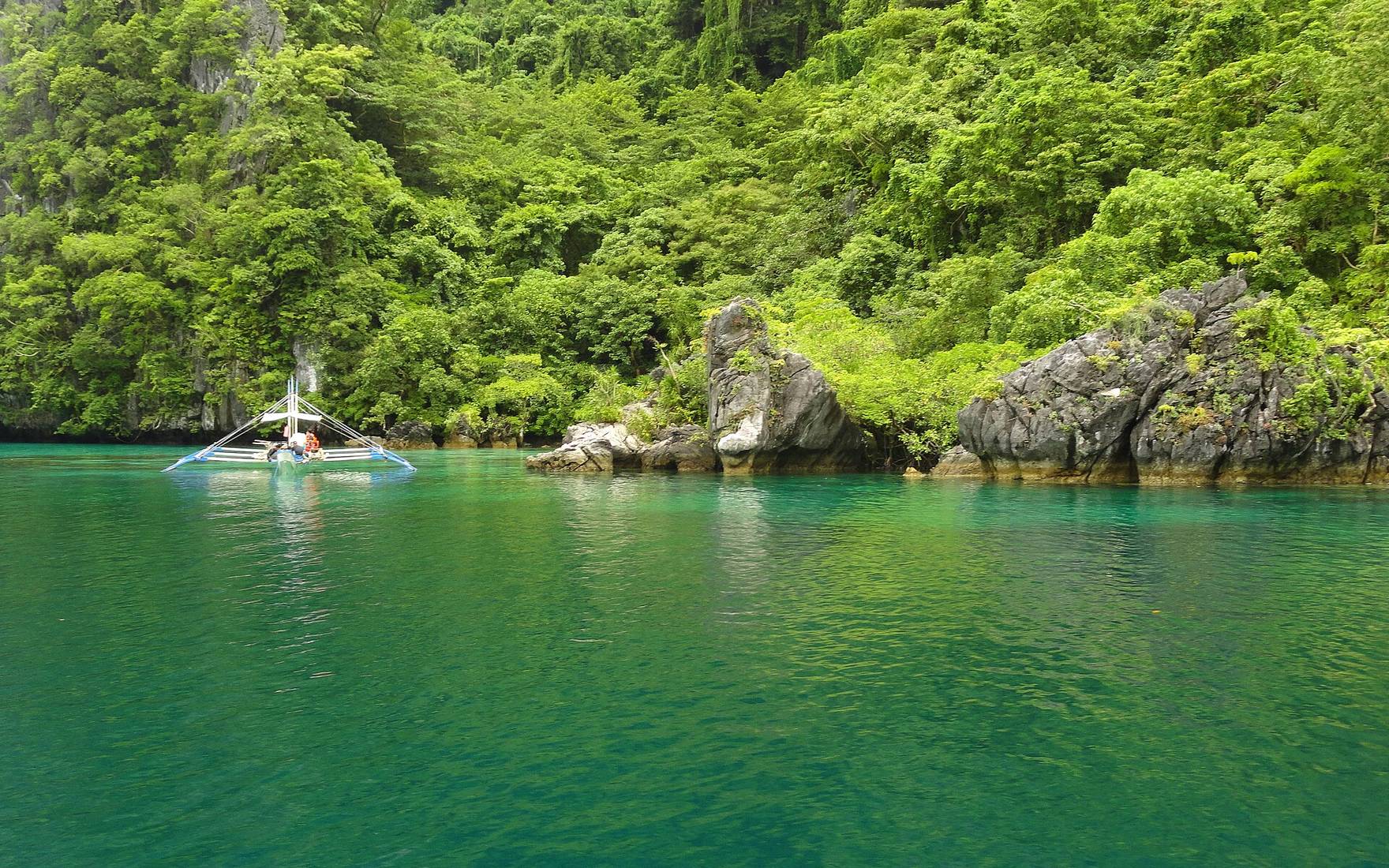 A small outrigger boat on emerald water under jungle-covered limestone, Big Lagoon, El Nido